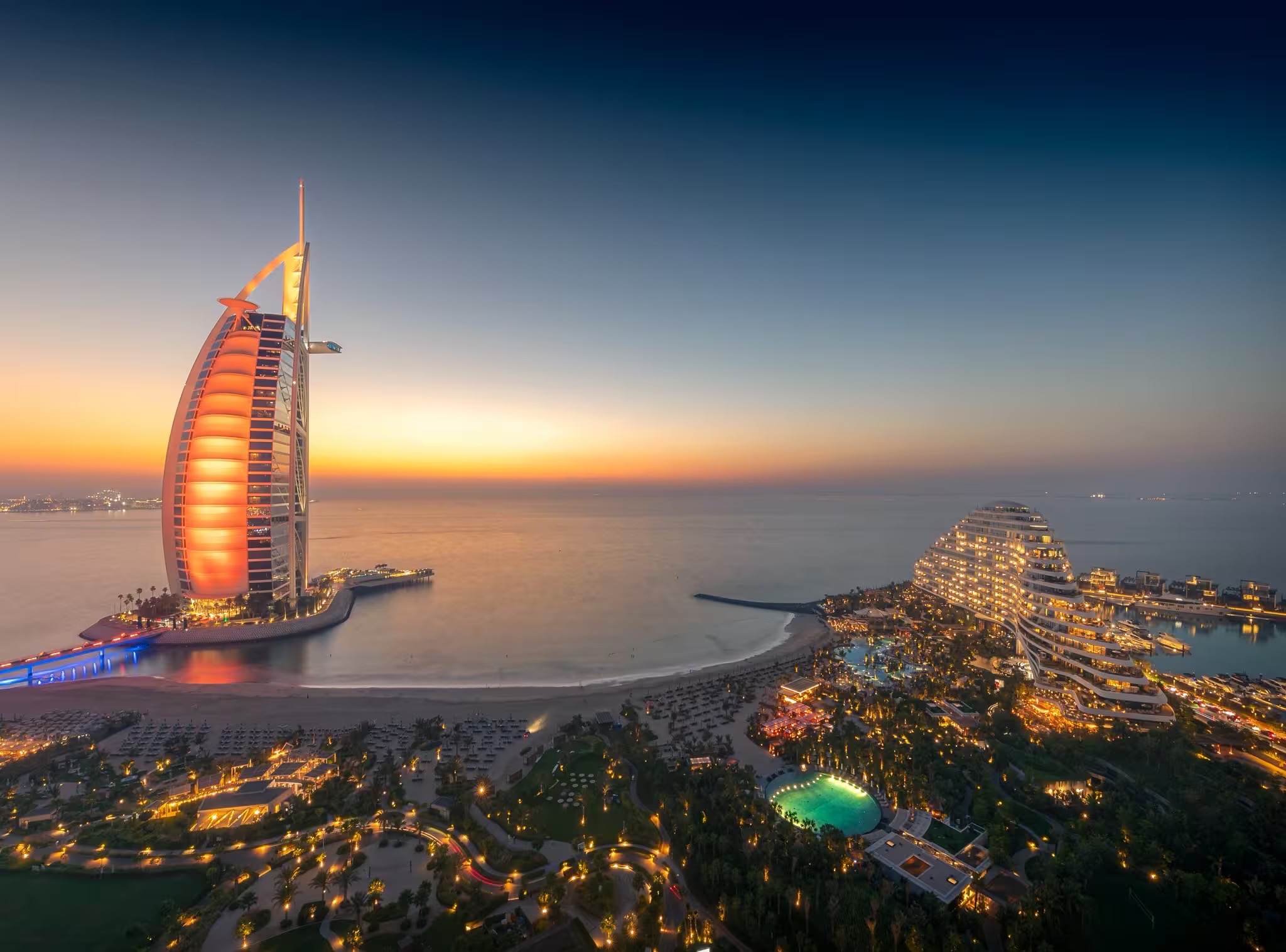 The Burj Al Arab on its island off the Jumeirah coastline, with Palm Jumeirah and the Dubai Marina skyline beyond.
